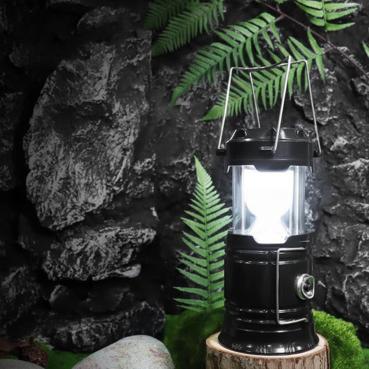 Soldriven campinglykta i svart med 360 graders LED-belysning på trästock i skogen